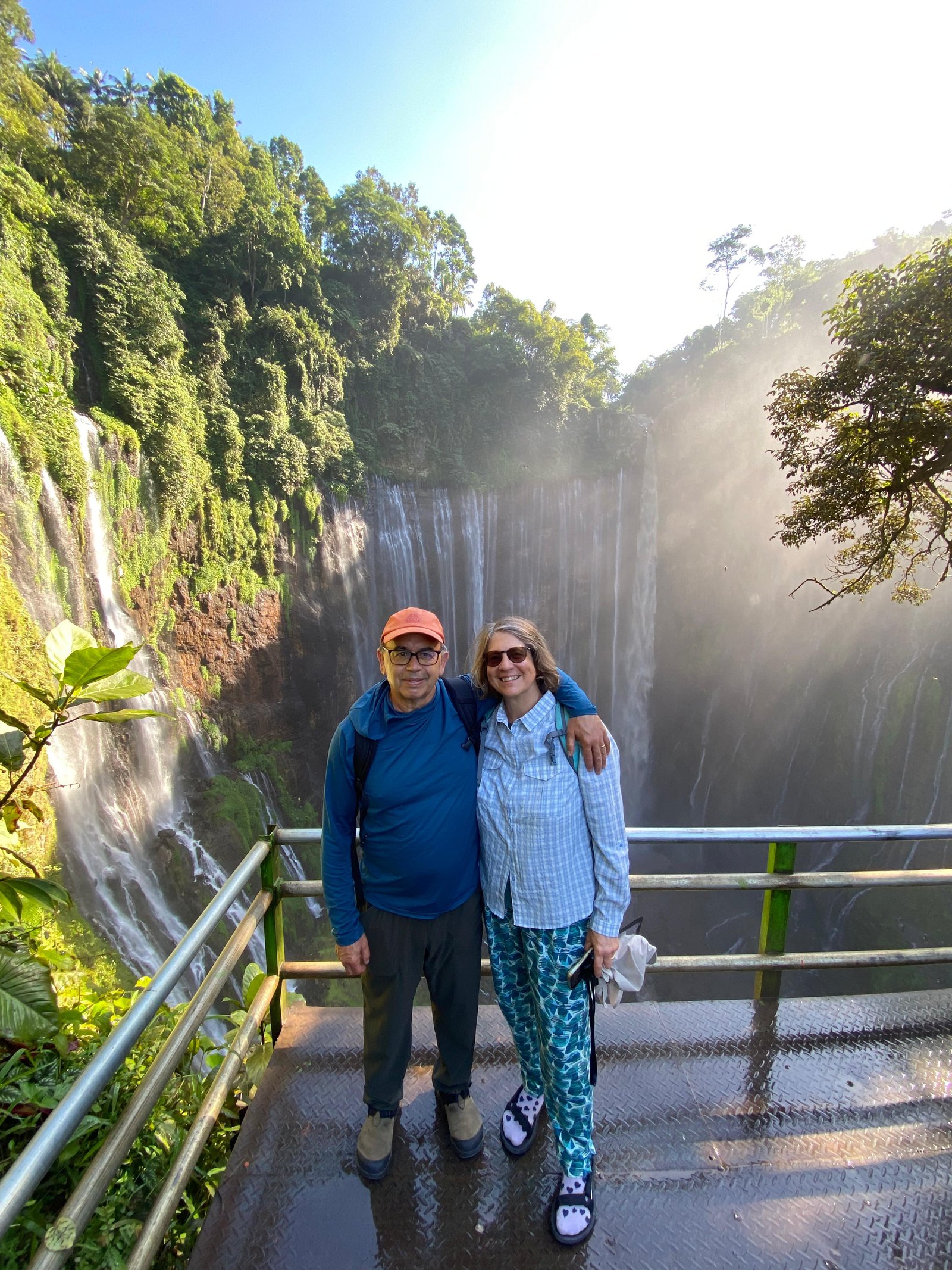 Travelers standing at the panoramic viewpoint overlooking the majestic Tumpak Sewu Waterfall in East Java, surrounded by lush tropical cliffs and cascading waterfalls.