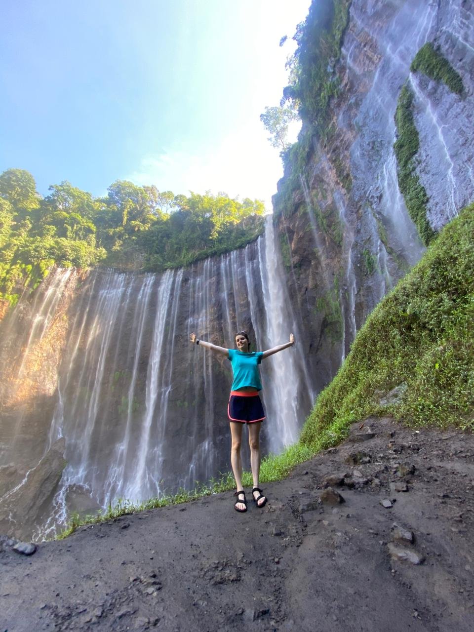 Travelers standing at the panoramic viewpoint overlooking the majestic Tumpak Sewu Waterfall in East Java, surrounded by lush tropical cliffs and cascading waterfalls.
