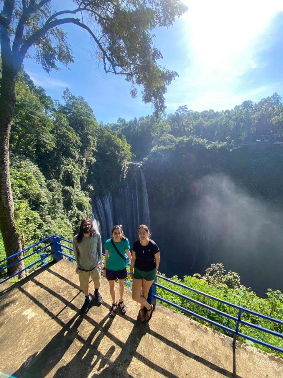 Travelers standing at the panoramic viewpoint overlooking the majestic Tumpak Sewu Waterfall in East Java, surrounded by lush tropical cliffs and cascading waterfalls.