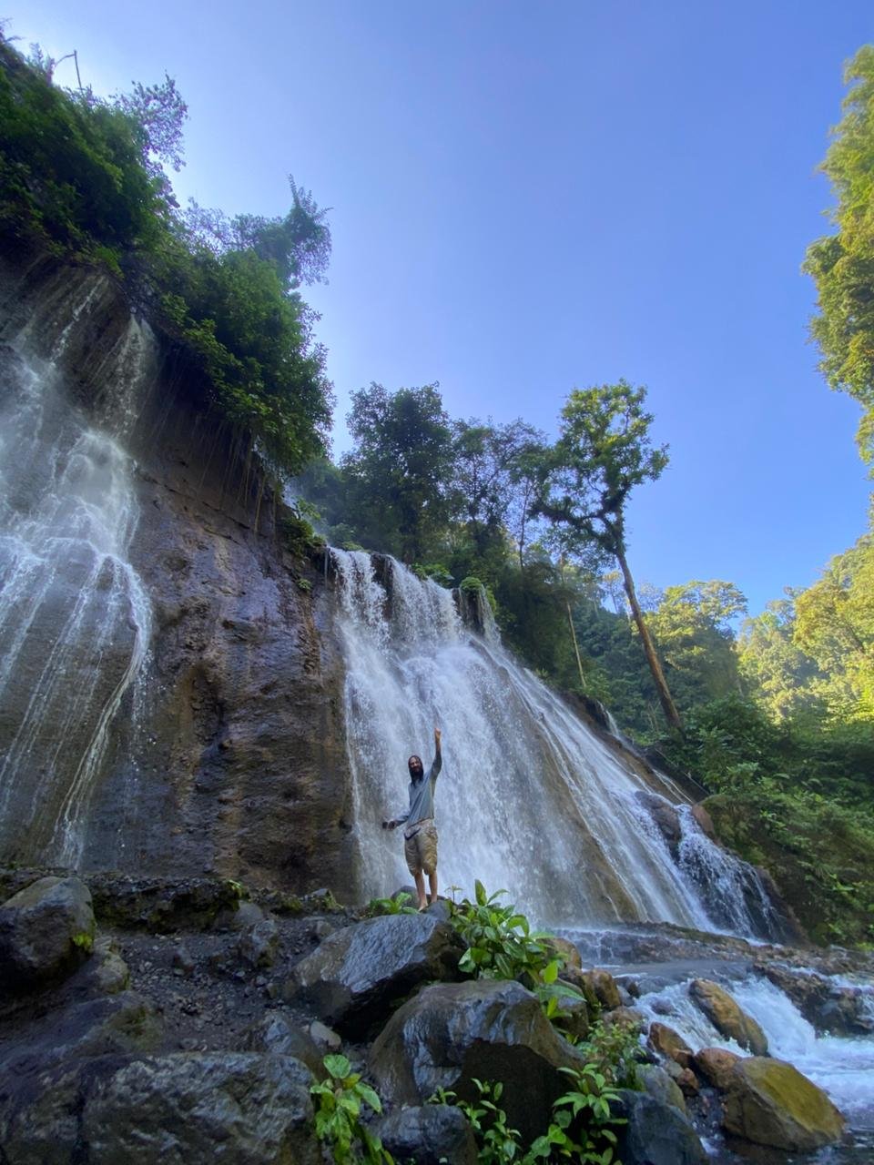 Travelers standing at the panoramic viewpoint overlooking the majestic Tumpak Sewu Waterfall in East Java, surrounded by lush tropical cliffs and cascading waterfalls.