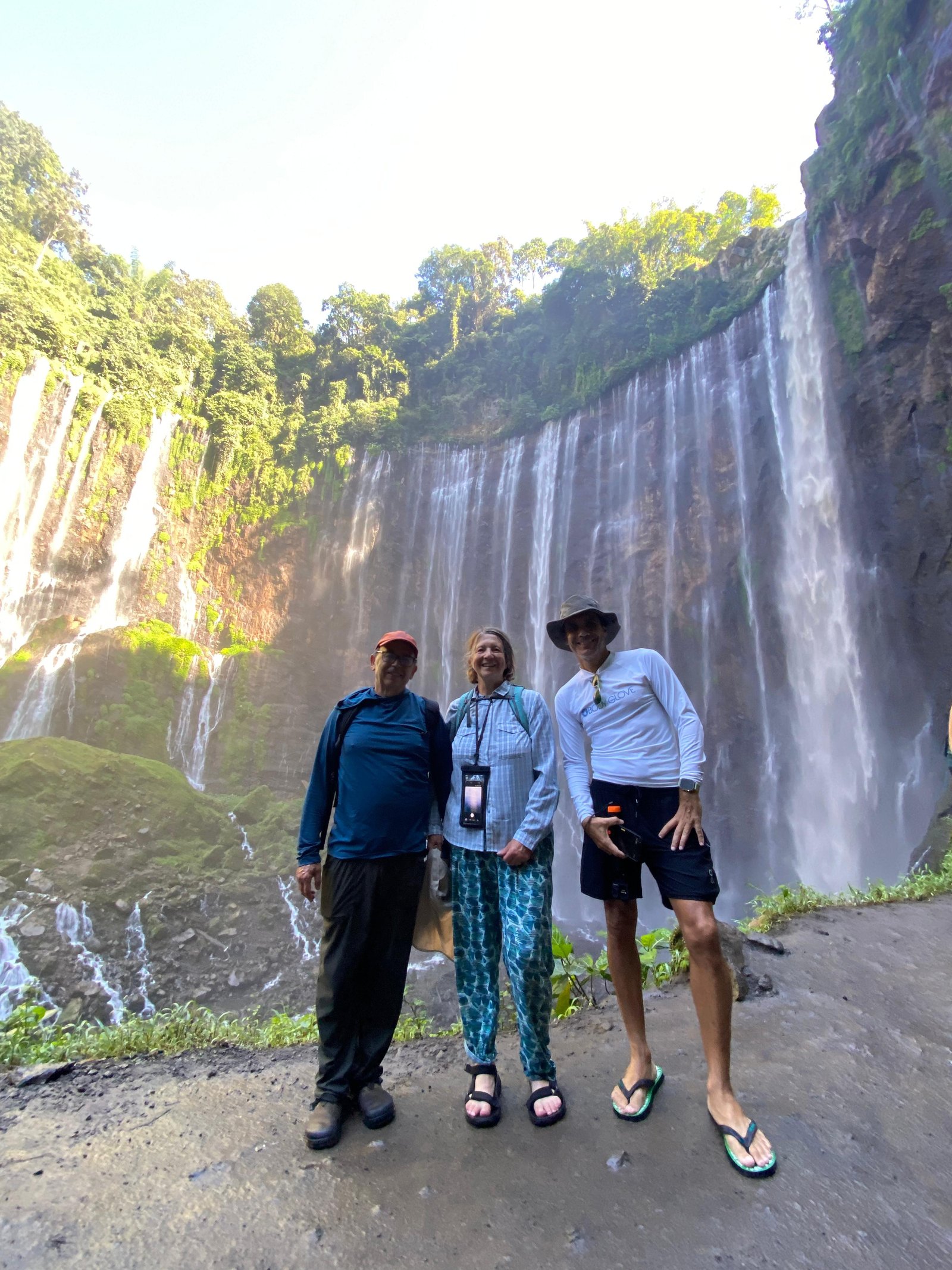 Travelers standing at the panoramic viewpoint overlooking the majestic Tumpak Sewu Waterfall in East Java, surrounded by lush tropical cliffs and cascading waterfalls.