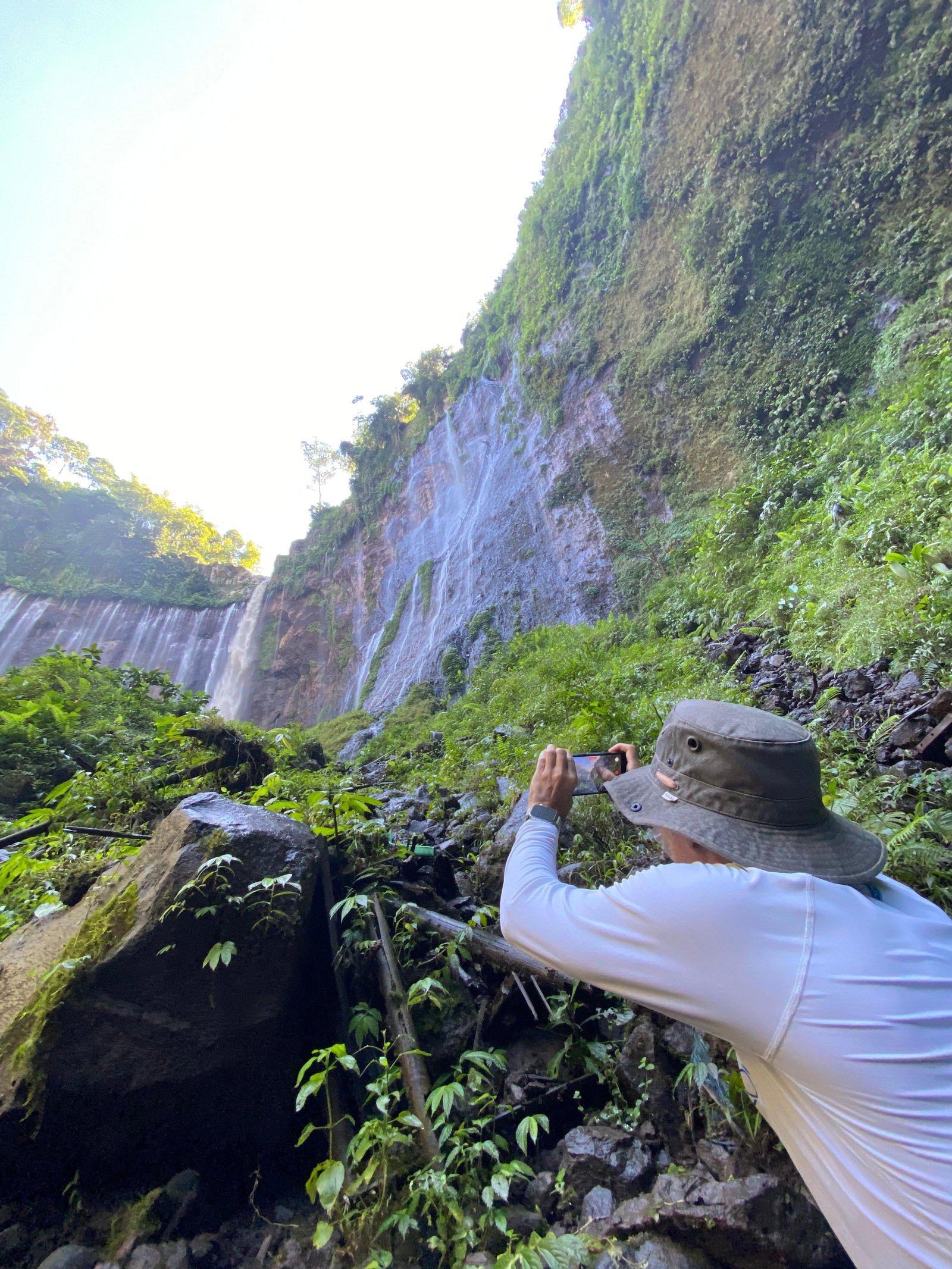 Travelers standing at the panoramic viewpoint overlooking the majestic Tumpak Sewu Waterfall in East Java, surrounded by lush tropical cliffs and cascading waterfalls.