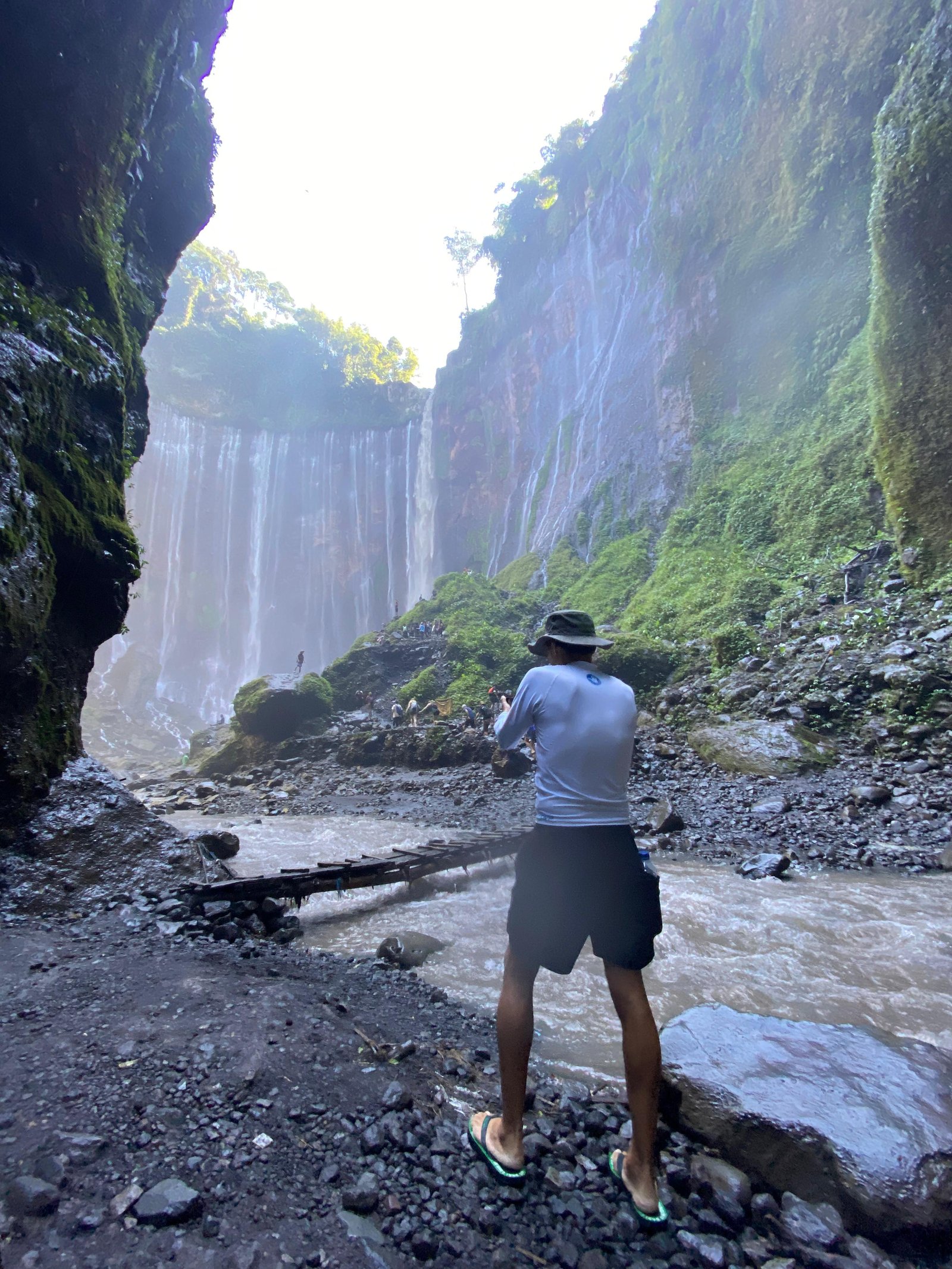 Travelers standing at the panoramic viewpoint overlooking the majestic Tumpak Sewu Waterfall in East Java, surrounded by lush tropical cliffs and cascading waterfalls.