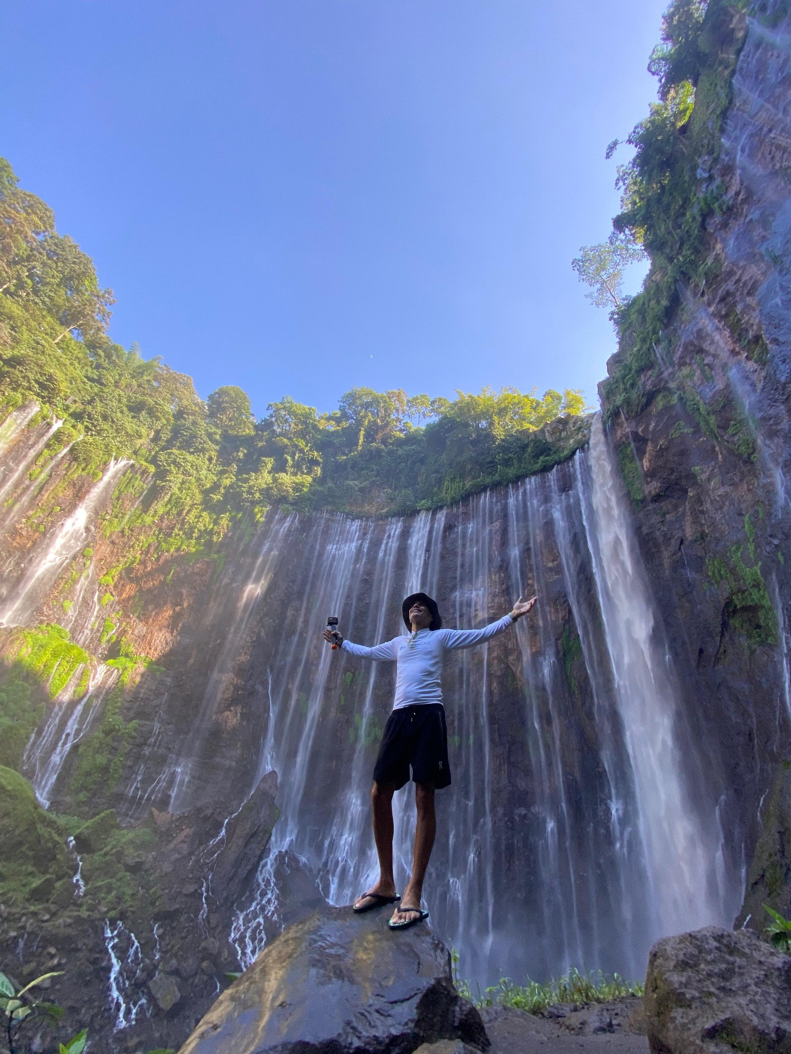 Travelers standing at the panoramic viewpoint overlooking the majestic Tumpak Sewu Waterfall in East Java, surrounded by lush tropical cliffs and cascading waterfalls.