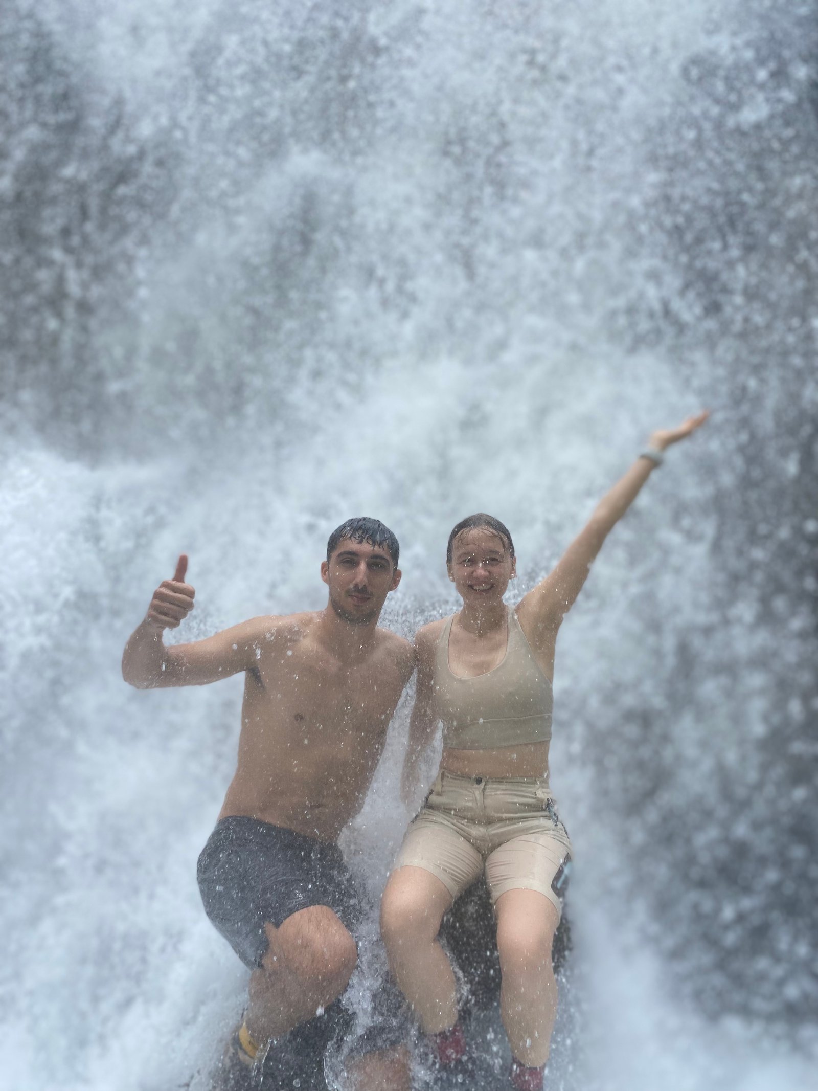 Travelers standing at the panoramic viewpoint overlooking the majestic Tumpak Sewu Waterfall in East Java, surrounded by lush tropical cliffs and cascading waterfalls.
