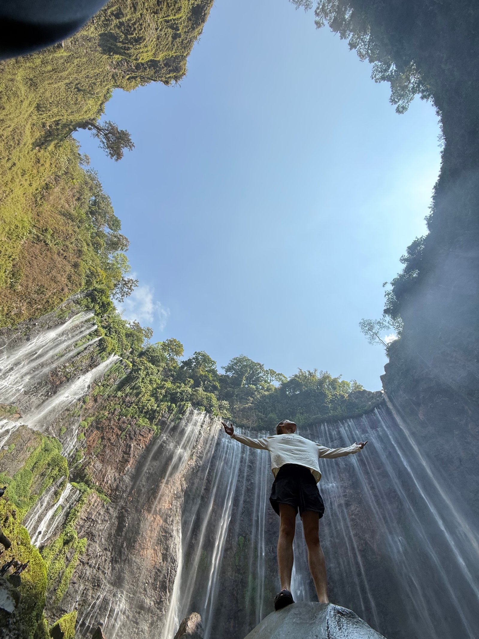 Travelers standing at the panoramic viewpoint overlooking the majestic Tumpak Sewu Waterfall in East Java, surrounded by lush tropical cliffs and cascading waterfalls.